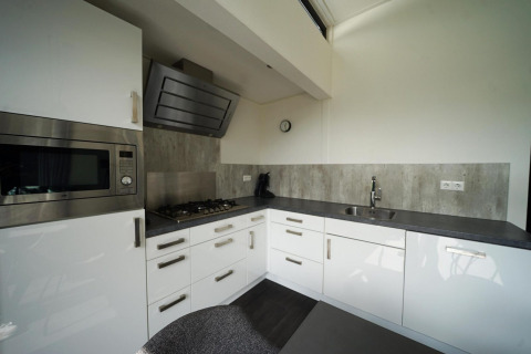 Cocina moderna en la cabaña L-Cube en Spaarnwoude, Países Bajos, con gabinetes blancos y encimera gris.