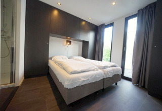 Moderne slaapkamer in L-Cube lodge Spaarnwoude, Nederland, met twee bedden en grote glazen deuren.