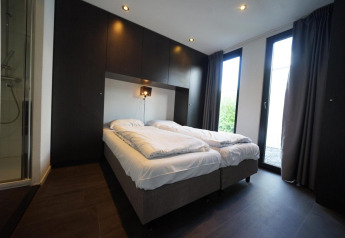 Moderne soveværelse i L-Cube lodge ved Spaarnwoude, Holland, med to senge og glasdør til haven.