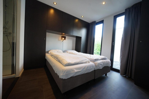 Moderne soveværelse i L-Cube lodge ved Spaarnwoude, Holland, med to senge og glasdør til haven.