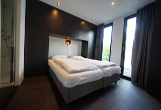 Moderne slaapkamer in de L-Cube lodge te Spaarnwoude, Nederland, met twee bedden en glazen deuren.