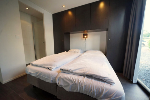 Moderne lodge slaapkamer met tweepersoonsbed, wit beddengoed en donkere kasten in L-Cube, Spaarnwoude, Nederland.