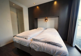Moderne lodge slaapkamer met tweepersoonsbed, wit beddengoed en donkere kasten in L-Cube, Spaarnwoude, Nederland.