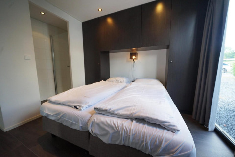 Moderne lodgekamer met dubbel bed, wit beddengoed en donkere kasten in L-Cube, Spaarnwoude, Nederland.
