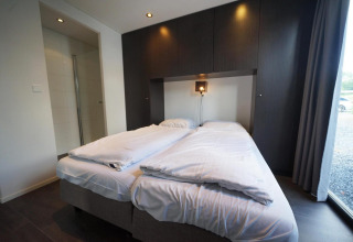 Moderne lodgekamer met dubbel bed, wit beddengoed en donkere kasten in L-Cube, Spaarnwoude, Nederland.