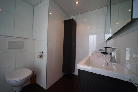 Baño moderno en la casa L-Cube en Spaarnwoude, Países Bajos, con inodoro mural y lavabo grande.