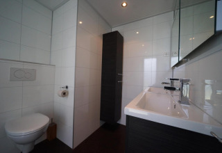 Baño moderno en la casa L-Cube en Spaarnwoude, Países Bajos, con inodoro mural y lavabo grande.