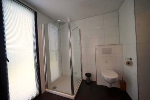 Moderne badkamer in L-Cube te Spaarnwoude, Nederland, met glazen douche, hangtoilet en groot raam.