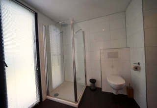 Moderne badkamer in L-Cube te Spaarnwoude, Nederland, met glazen douche, hangtoilet en groot raam.