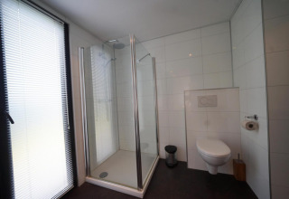 Salle de bain moderne au L-Cube à Spaarnwoude, Pays-Bas, avec douche, WC suspendu et grande fenêtre.