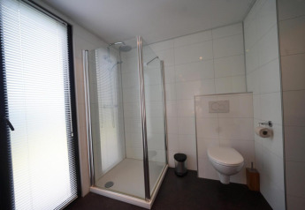 Moderne badeværelse i L-Cube på Spaarnwoude, Holland, med brusekabine, vægmonteret toilet og stort vindue.