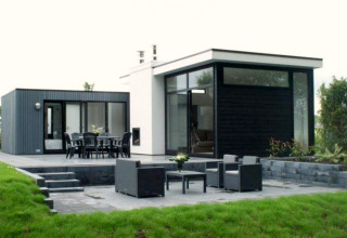 Moderne L-Cube lodge bij Spaarnwoude in Nederland met terras, grote ramen en uitzicht op de tuin.