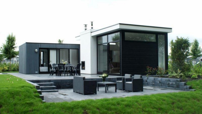Moderne L-Cube-Lodge in Spaarnwoude, Niederlande, mit Terrasse, großen Fenstern und Gartenansicht.