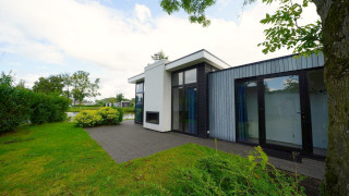 Buitenfoto van Cube Maximaal lodge met modern design, grote ramen, terras en tuin aan het water.
