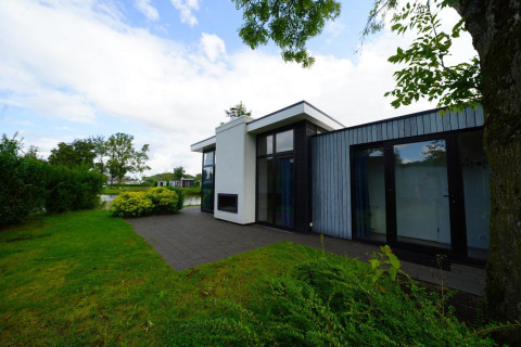 Buitenfoto van Cube Maximaal lodge met modern design, grote ramen, terras en tuin aan het water.