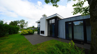 Photo extérieure de la lodge Cube Maximaal avec design moderne, grandes fenêtres et jardin au bord de l’eau.