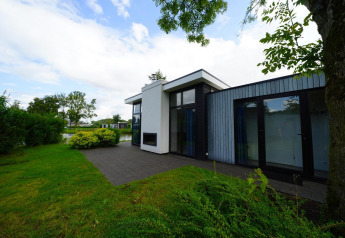 Outdoor photo of Cube Maximaal lodge with modern design, large windows, patio, and garden by the water.