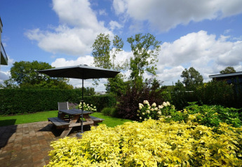 Giardino con fiori, arbusti verdi e terrazza con tavolo da picnic e ombrellone al Cube Maximaal a Spaarnwoude.