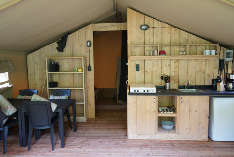 Innenansicht eines Safari-Zeltes mit Küchenzeile, Essbereich und Regalen auf Camping Pittoresque in Frankreich.