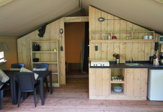 Interieur van een safaritent met keuken, eettafel en rekken op Camping Pittoresque in Frankrijk.