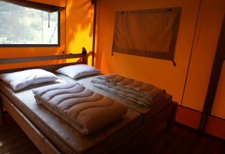 Interior de una tienda safari con colchones, almohadas y edredones en Camping Pittoresque, Francia.