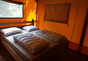 Interno di una tenda safari con materassi, cuscini e piumoni al Camping Pittoresque in Francia.