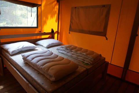 Innenansicht eines Safarizelts mit Doppelbett, Kissen und Decken im Camping Pittoresque, Frankreich.