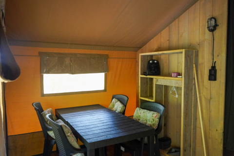 Innenansicht eines Safari-Zeltes mit Esstisch, Stühlen und Regal im Camping Pittoresque, Frankreich.