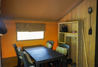 Indendørs udsigt over Safari-teltet med spisebord, fire stole, hylder og vindue på Camping Pittoresque.