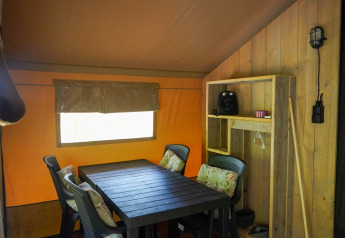 Innenansicht eines Safari-Zeltes mit Esstisch, Stühlen und Regal im Camping Pittoresque, Frankreich.