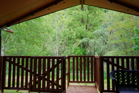 Blick von der Veranda eines Safarizelts auf Camping Pittoresque in Frankreich mit grünem Wald dahinter.