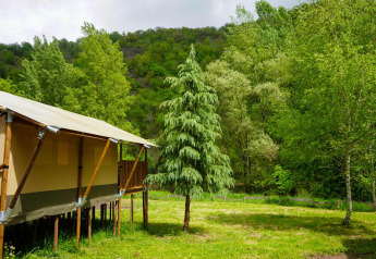 Tienda safari con baño privado en Camping Pittoresque, Francia, rodeada de árboles verdes y colinas.