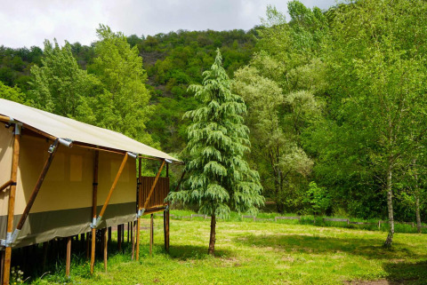 Safari-Zelt mit eigenem Bad auf Camping Pittoresque in Frankreich, umgeben von grünen Bäumen und Hügeln.