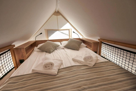 Cama doble con almohadas y toallas dentro de Glampingtent en Reestervallei, Países Bajos, ambiente acogedor.