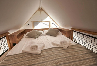 Cama doble con almohadas y toallas dentro de Glampingtent en Reestervallei, Países Bajos, ambiente acogedor.