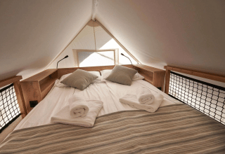 Cozy bedroom with double bed and pillows inside Glampingtent at Reestervallei, Netherlands, natural light.