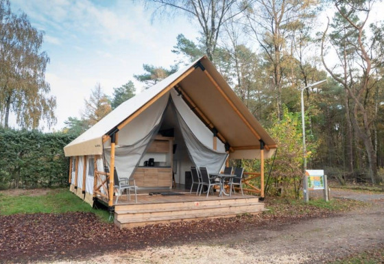Tienda safari con porche cubierto y muebles de exterior, rodeada de naturaleza y árboles para glamping.