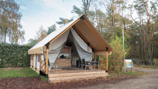 Tienda safari con porche cubierto y muebles de exterior, rodeada de naturaleza y árboles para glamping.
