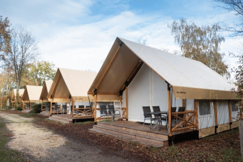 Row of modern safari tents with wooden decks and outdoor chairs on a peaceful, wooded campground.