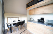 Interior view of a safari tent featuring a modern kitchen, dining table, and black chairs on wooden flooring.