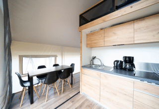 Interieur van een safaritent met moderne keuken, eettafel en zwarte stoelen op een houten vloer.