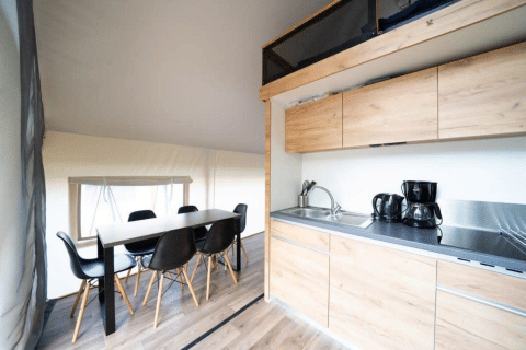 Binnenaanzicht van een safaritent met moderne keuken, eettafel en zwarte stoelen op houten vloer.