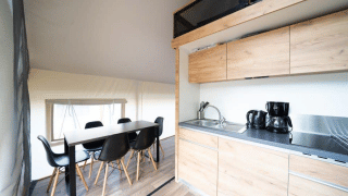 Vista interna di una tenda safari con cucina moderna, tavolo da pranzo e sedie nere su pavimento in legno.