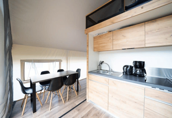 Vista interna di una tenda safari con cucina moderna, tavolo da pranzo e sedie nere su pavimento in legno.