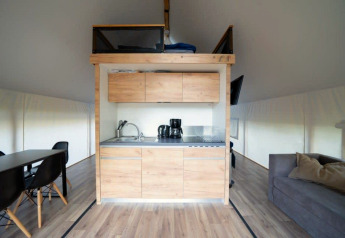 Moderne safaritent met kleine keuken, eethoek, bank en houten vloer in lichte en open opstelling.