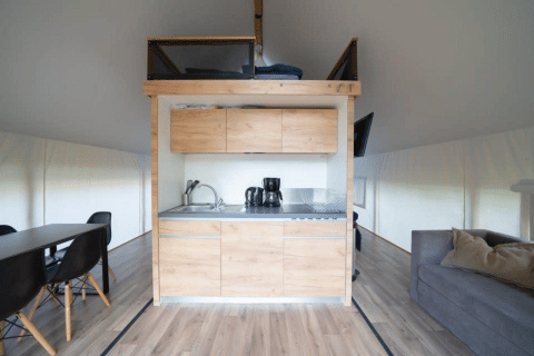Intérieur d’une tente safari moderne avec kitchenette, espace repas, canapé et sol en bois.