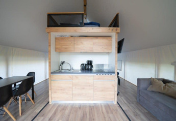 Moderne indretning i safaritelt med lille køkken, spiseområde og sofa med puder på trægulv.