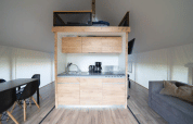 Intérieur d’une tente safari moderne avec kitchenette, espace repas, canapé et sol en bois.