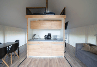 Moderne safaritent met kleine keuken, eethoek, bank en houten vloer in lichte en open opstelling.