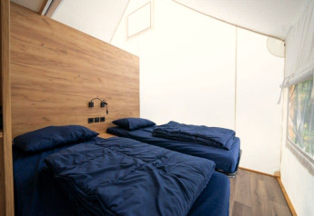 Binnenaanzicht van een safaritent met twee eenpersoonsbedden, houten wand en zijraam.